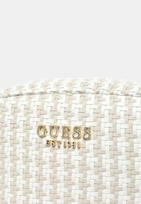 Borsa intrecciata in beige e bianco. Presenta il logo "GUESS" in tonalità oro e la data di fondazione, con un motivo a trama incrociata.