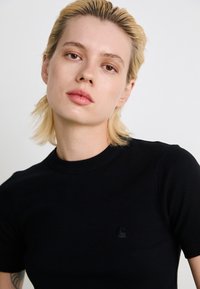 Sort ribbet kortærmet t-shirt med rund halsudskæring og et lille, tonalt bølgelogo på brystet. Glat stofstruktur.