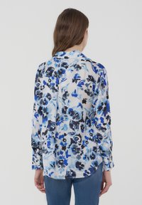 Blusa a maniche lunghe floreale in tonalità blu e nere. Tessuto leggero e trasparente con una vestibilità morbida, caratterizzata da un colletto e polsini con bottoni.