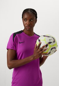 Purple Nike sports jersey with short sleeves, black shoulder accents. Female figure holding a white and green patterned soccer ball.