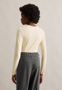 Top de manga comprida, amarelo claro, combinado com calças cinza carvão com riscas finas, apresentando uma cintura elástica e um bolso traseiro.