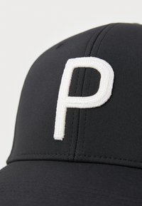 Čierna čiapka so štruktúrovaným dizajnom, na prednej strane je biele vyšívané písmeno "P". Vyrobená z hladkej látky s viditeľným švom.