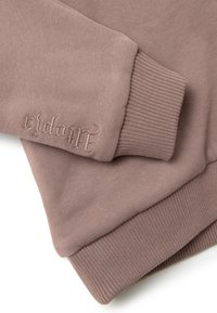 Felpa taupe con polsini e orlo a costine, con testo del marchio ricamato in un font decorativo sul polsino, texture del tessuto liscia.