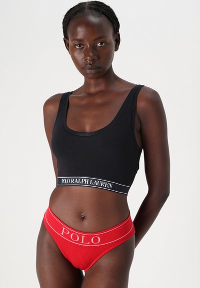 Μαύρο βαμβακερό cropped top με λευκή ζώνη λογότυπου και κόκκινο ριμπ εσώρουχο με λευκή ζώνη λογότυπου, παρουσιασμένο σε μοντέλο.