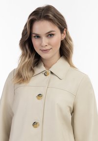 Beige Lederjacke mit klassischem Kragen, vier großen Knöpfen mit glänzendem Finish und glatter Textur.