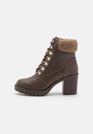 Bottine en cuir marron avec talon épais, fermeture à lacets devant avec œillets dorés et col en fausse peau retournée plié.