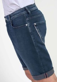 Shorts de mezclilla en azul oscuro con una textura suave, diseño de cinco bolsillos, dobladillo vuelto y detalles de costura en contraste. Cierre de botón.
