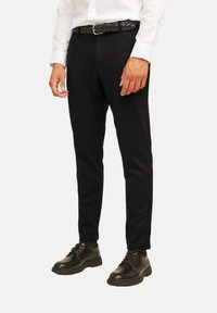 Pantalones negros con un corte entallado, combinados con un cinturón de cuero trenzado negro y zapatos de cuero negros, presentando un aspecto pulido.