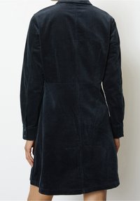 Abito in corduroy blu scuro con colletto, maniche lunghe e polsini con bottoni. Presenta una texture a coste e una silhouette sagomata.