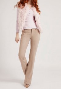 Gilet di pelliccia finta rosa chiaro sopra una morbida camicia a maniche lunghe rosa, abbinato a pantaloni beige a zampa d'elefante e tacchi rosa chiaro impreziositi.