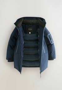 Parka en bleu marine avec doublure isolante, fermeture éclair à l'avant, intérieur rembourré et poches latérales. Présente une étiquette logo et des rayures contrastées.