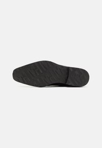 Semelle en caoutchouc noir avec un motif texturé pour une meilleure adhérence, un design légèrement courbé et des bords lisses.