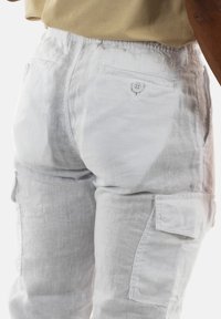 Weiße Leinencargo-Hosen mit einem Kordelzugbund, zwei Fronttaschen und einer zusätzlichen Seitentasche. Der Stoff hat eine natürliche Struktur.