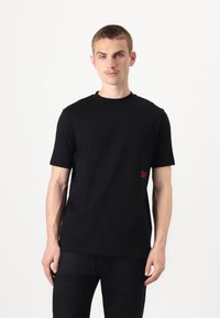 Svart t-skjorte med korte ermer laget av bomull, med rund hals og røde aksentdetaljer på venstre side. Fitted design med en glatt tekstur.
