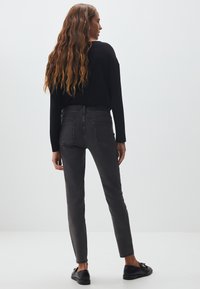 Jeans gris slim-fit avec taille mi-haute, présentant un design classique à cinq poches et des détails de couture. La vue arrière montre un léger délavage.