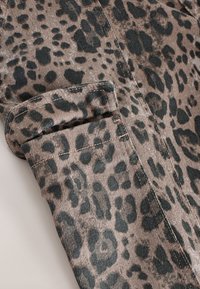 Leopardmuster-Stoff mit einer strukturierten, Cord-Oberfläche. Verfügt über eine umgeschlagene Manschette und kontrastierende Nähte in einem dunkleren Ton.