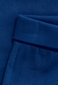 Nahaufnahme eines blauen gerippten Bündchens, das über einen glatten blauen Stoffhintergrund gefaltet ist.