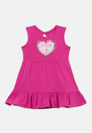 Różowa sukienka dla malucha bez rękawów, z falbanką na dole i cekinową naszywką w kształcie serca z napisem "GUESS U.S.A." z przodu.