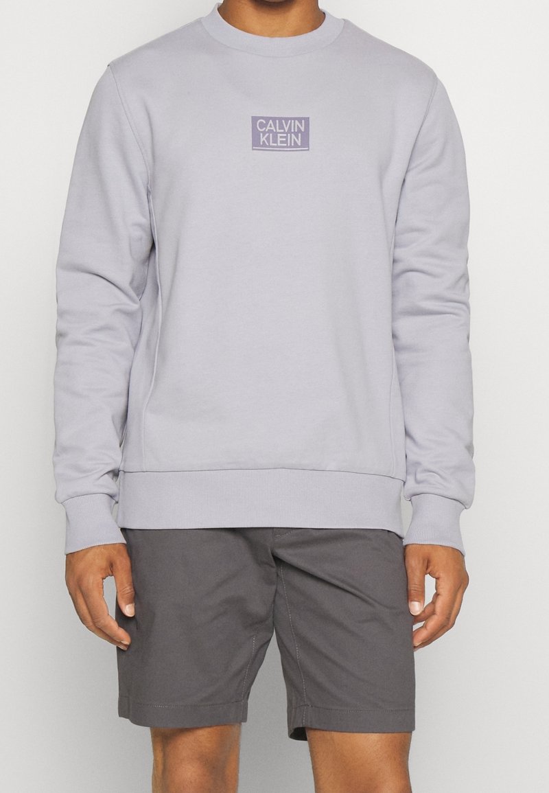 Ljuslila sweatshirt med rund halsringning, långa ärmar och ribbade muddar. Har en liten Calvin Klein-logotyp i en rektangulär ruta på bröstet.