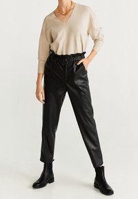 Beżowy sweter z dekoltem w serek zestawiony z czarnymi skórzanymi spodniami dresowymi z marszczonym pasem. Czarne botki za kostkę dopełniają outfit.
