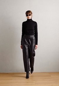 Black turtleneck top paired with high-waisted, wide-leg leather pants. Model wears sleek black sunglasses and pointed ankle boots.