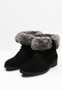 Bottines en daim noir avec un poignet en fausse fourrure grise, lacets à l'avant et un talon bas et plat. Texture douce avec un design épuré et minimaliste.