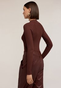 Top marrone a maniche lunghe con costine, colletto alto, forma aderente, abbinato a pantaloni in pelle bordeaux a vita alta. Texture liscia.