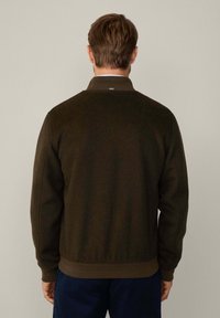 Dark green, textured jacket with a ribbed hem and cuffs. Features a collar, visible stitching, and a small tag on the back.