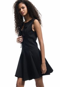 Schwarzes ärmelloses Kleid aus glattem Stoff, mit einem taillierten Oberteil, plissiertem Rock und einer dekorativen Schleife am Ausschnitt.