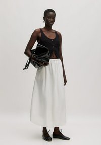 Schwarzes, kurzes Tanktop mit Knöpfen, weiße Knöchellange Rock und eine glänzende schwarze Handtasche. Getragen mit schwarzen Schnürschuhen.