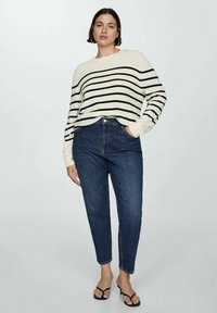 Maglione a righe in crema e nero, colletto rotondo, vestibilità rilassata, abbinato a jeans blu a vita alta, completato con infradito nere.
