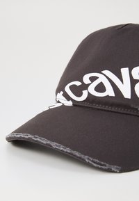 Svart baseballcap i teksturert stoff, med fremtredende hvit merkevare på fronten og en litt slitt skjermkant.