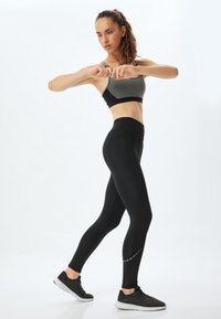 Zwarte high-waisted legging met een gladde textuur en reflecterende accenten. Grijze sportbh met een modern ontwerp, aansluitende en cropstijl.
