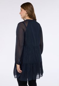 Granatowa, długorękawowa sukienka z warstwowym, falbankowym dołem i przezroczystą fakturą. Posiada okrągły dekolt i elastyczne mankiety przy rękawach.