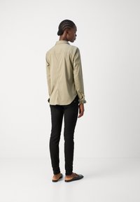 Camisa beige com colarinho, mangas longas e punhos franzidos, combinada com calças pretas skinny e sapatos deslizantes pretos.