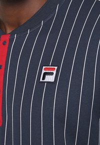 Marinrandig polo skjorta med röd accent och knappar, tillverkad av bomull. Har broderad FILA-logotyp på vänster bröst.