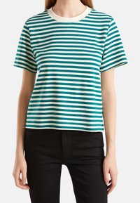 Randig t-shirt i teal och vitt, kortärmad, rundad halsringning, tillverkad av mjukt tyg med en avslappnad passform. Svarta jeans synliga vid midjan.