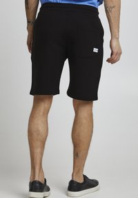 Pantaloni scurți negri din material moale, cu talie elastică, o singură buză la spate și un mic eticheta cu logo. Lungime până la mijlocul coapsei.