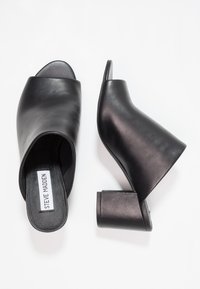 Zwarte leren open-tegen muiltjes met een gestructureerd ontwerp, voorzien van een lage, blokhak en een gladde textuur. Merkenlabel zichtbaar aan de binnenkant.