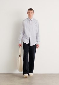 Lyseblå langermet skjorte, mørke vidde bukser og beige totebag. Glatt tekstur, knappefront, ensfarget design og nøytrale farger.