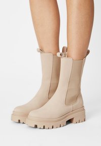 Beige Stiefeletten aus glattem Wildleder mit elastischen Seitenpaneelen und einer dicken Gummisohle mit strukturiertem Profil. Doppelte Zuglaschen oben.