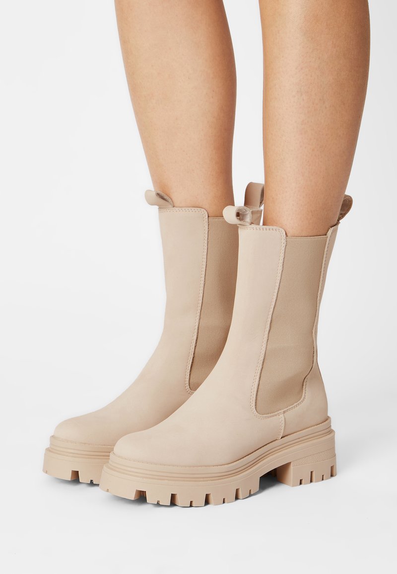 Beige Stiefeletten aus glattem Wildleder mit elastischen Seitenpaneelen und einer dicken Gummisohle mit strukturiertem Profil. Doppelte Zuglaschen oben.