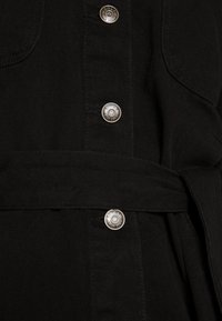 Vestido de mezclilla negra con herrajes de botón plateados, cinturón envolvente y tejido texturizado con dos bolsillos frontales.