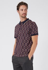 Polo de manga corta hecho de tela estampada con formas de diamante en color burdeos, crema y azul marino, con un cuello en contraste.
