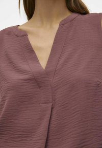 Halenka bez rukávů s výstřihem do V v texturované mauve látce, s jemným skladem na výstřihu a uvolněným střihem.