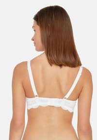 White lace bra with adjustable straps, scalloped edges, and a hook-and-eye closure at the back, showcasing intricate lace details.