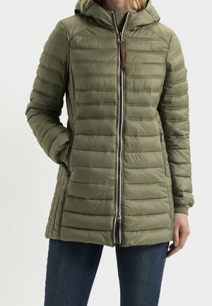 Femme portant une veste matelassée à capuche vert olive avec fermeture éclair devant et poches latérales, associée à un jean bleu foncé.