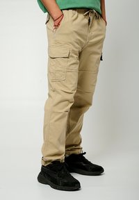 Beige cargobroek met een elastische tailleband, voorzakken en cargozakken aan de zijkanten. Gekocht met zwarte sneakers.