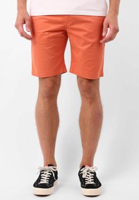 Shorts en coton orange avec un devant plat, des poches latérales et arrière, et un ourlet propre, associés à des baskets noires.