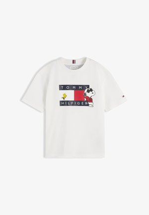 Jeune fille avec deux couettes bouffantes portant un t-shirt blanc à motif Snoopy, un jean foncé et des baskets blanches, debout les mains jointes.
